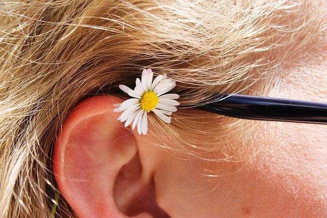 Oor met zwarte bril, blond haar en madeliefje.