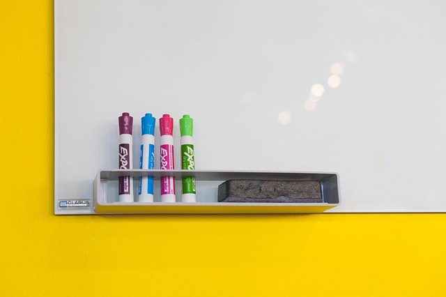 gele wand met white board, daarop ene rijtje met 4 gekleurde stiften.