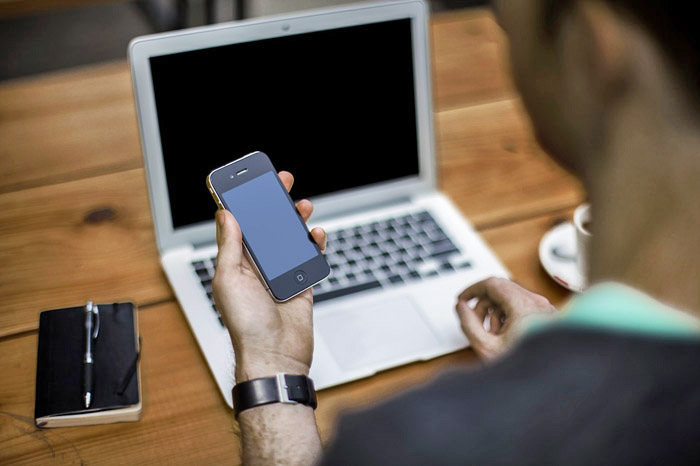 man op de rug gezien met smartphone in zijn hand, achter laptop.