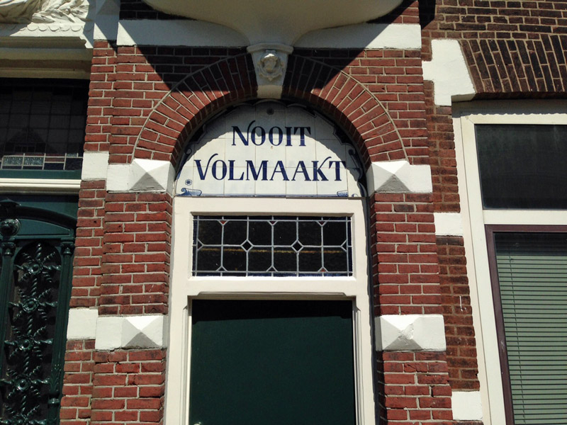 toegangsdeur van historisch huis, met tekst in tegels erboven: Nooit Volmaakt.