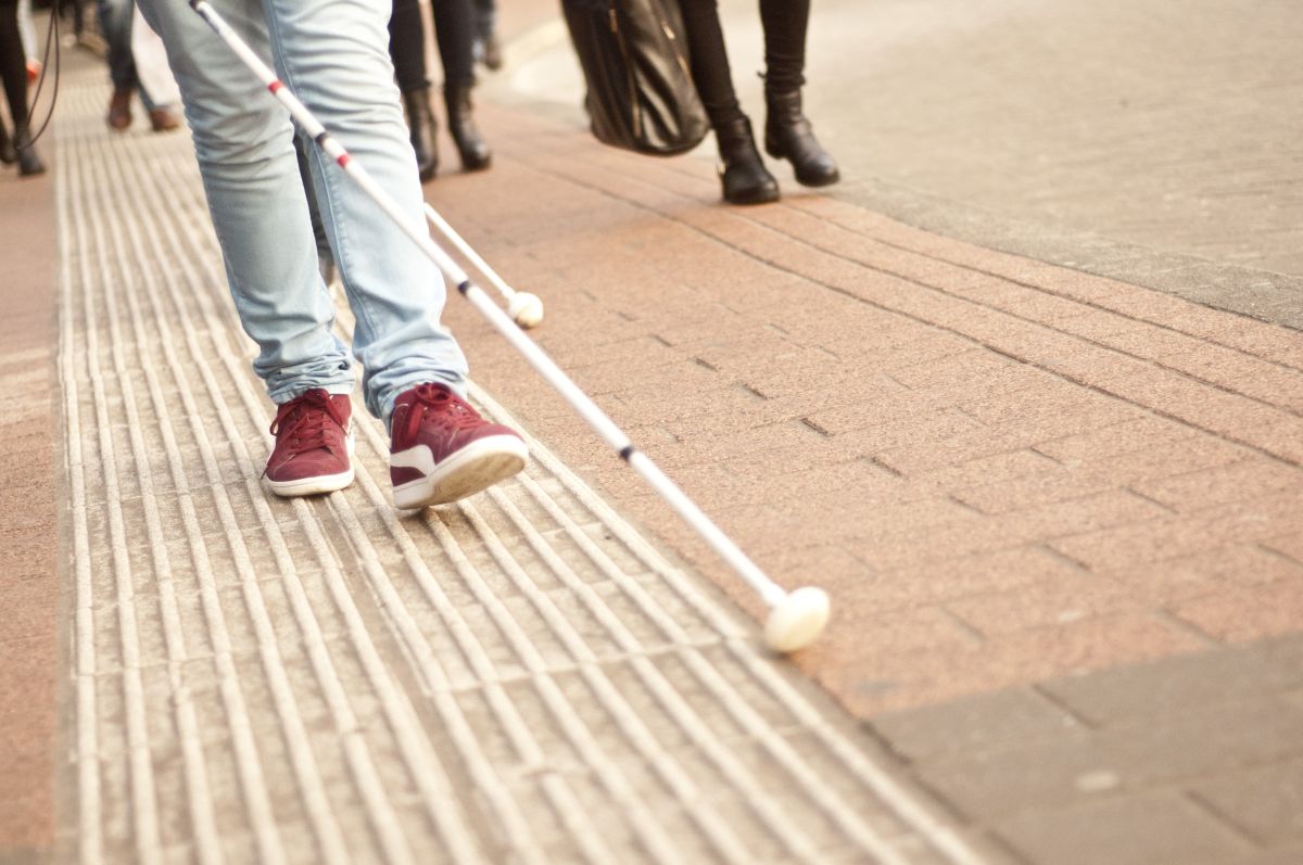 Persoon loopt met witte stok over straat