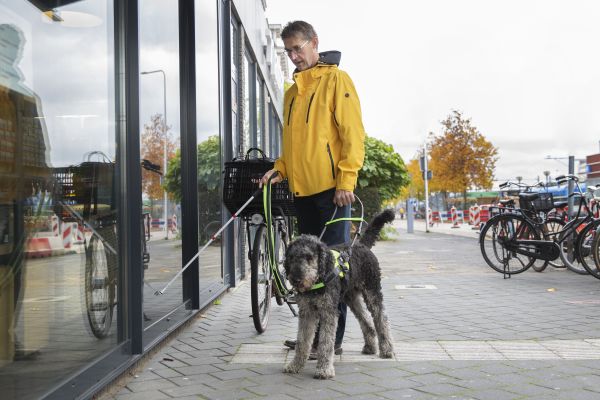 Man met stok en geleidehond komt aan bij ingang station