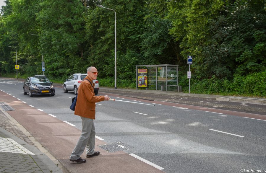 Man met stok steekt straat over