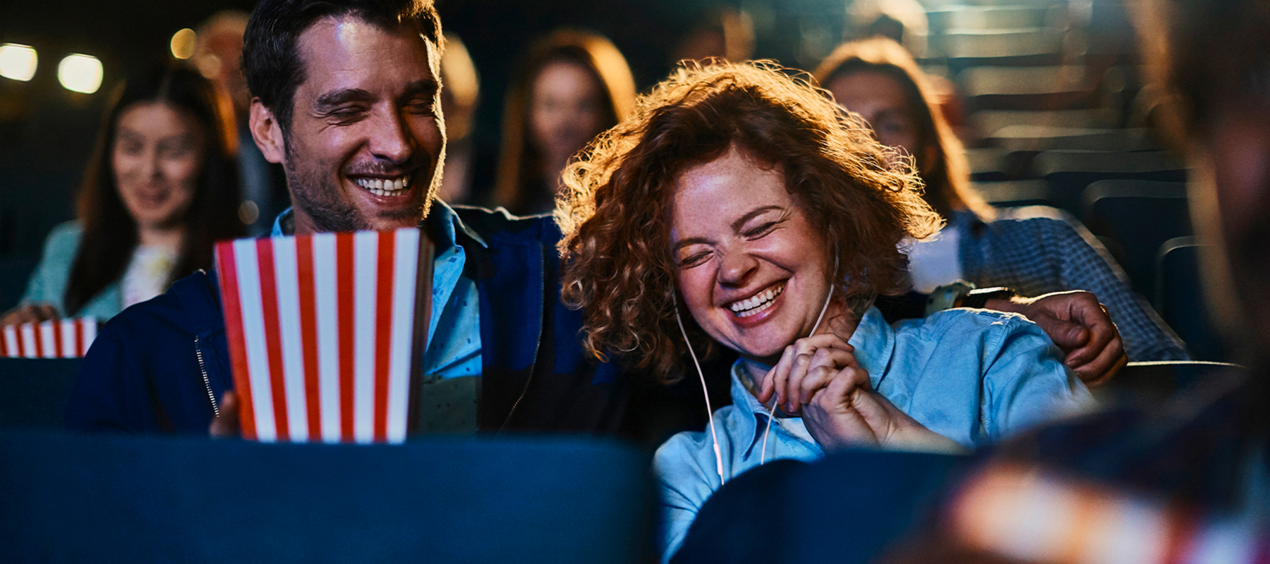 Man en vrouw genieten samen van een film in de bioscoop, vrouw heeft oortjes in voor audiodescriptie.