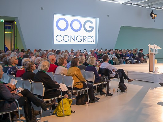 Volle zaal met mensen met aan de wand een scherm met logo Oogcongres