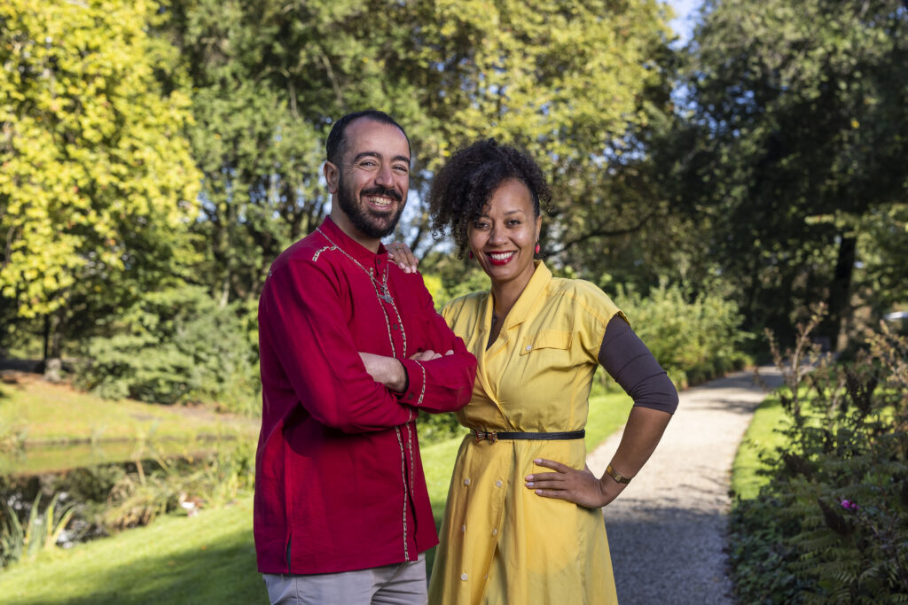 Man met rood shirt en vrouw met gele jurk staan lachend samen voor een parkachtige achtergrond