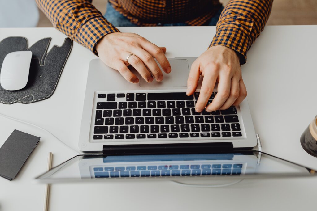 Bovenaanzicht van opengeslagen laptop op tafel. 2 handen zichtbaar op toetsenbord