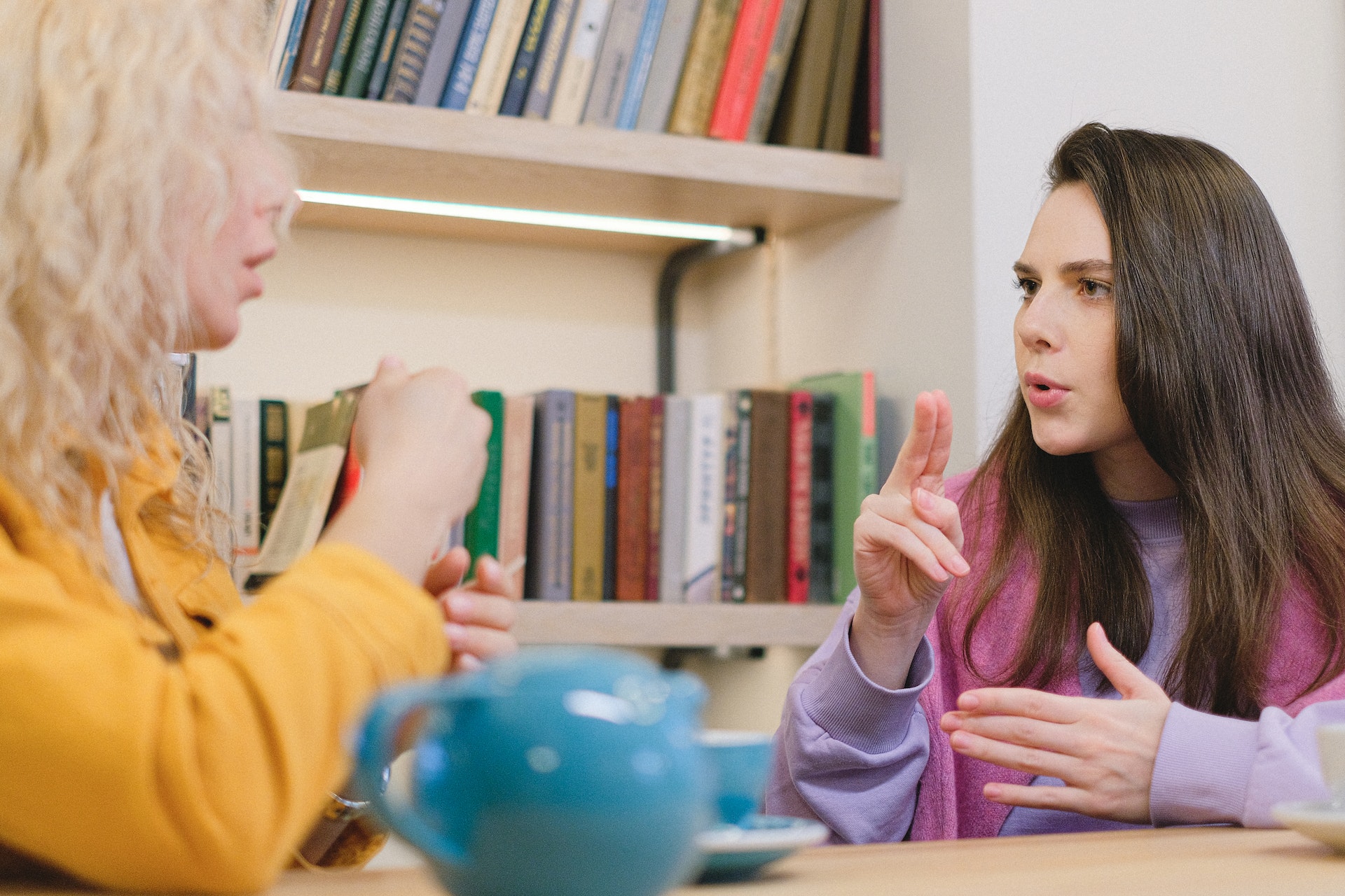 Twee jonge vrouwen spreken gebarentaal met elkaar aan tafel in een café.