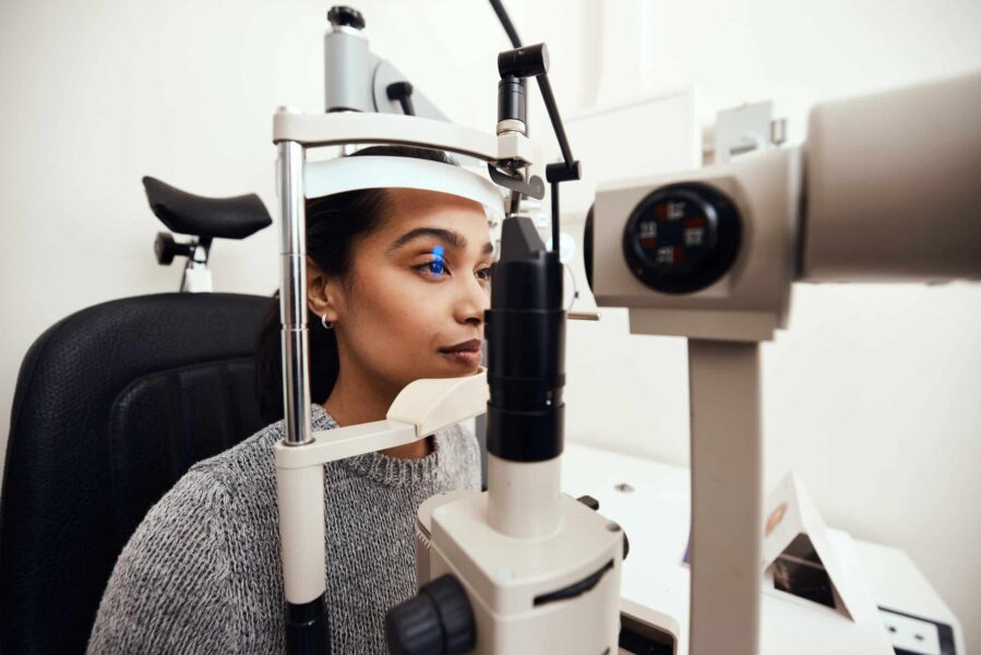 Een jonge vrouw zit en drukt met haar voorhoofd en kin tegen een apparaat om haar oog te laten meten door de opticien.