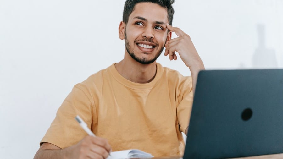 Student met licht oranje shirt met pen en papier achter zijn laptop