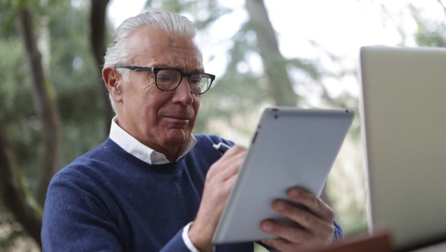 Oudere man met bril scrollt op zijn tablet
