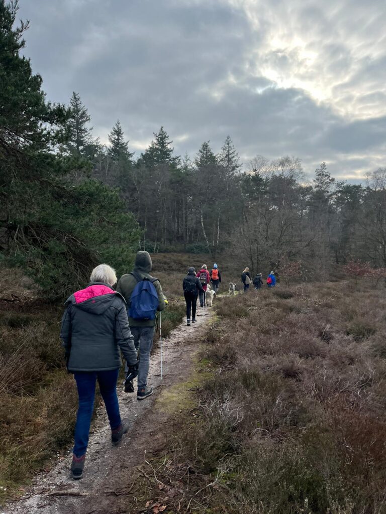 Mensen lopen op een smal heidepaadje achter elkaar aan