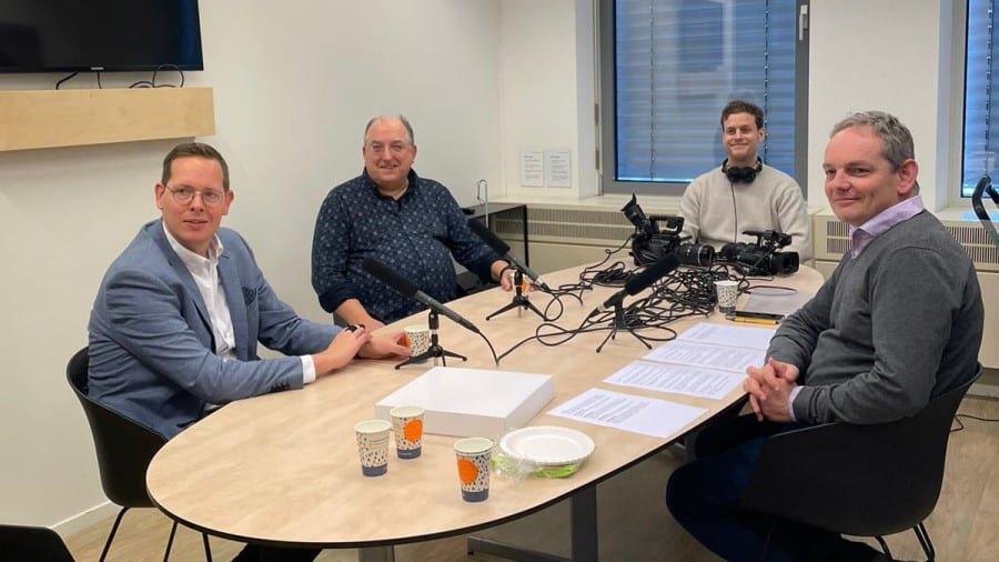 Vier mensen zitten aan tafel om de podcast op te nemen