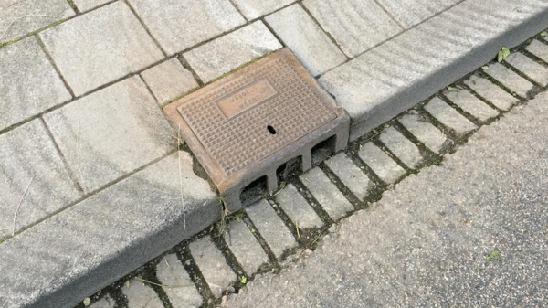 een stoep langs een straat met regenafvoerput