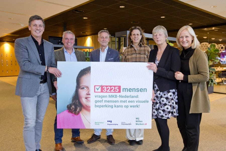 Foto overhandiging petitie. Mensen staan op een rij en laten een bord met de petitie zien.