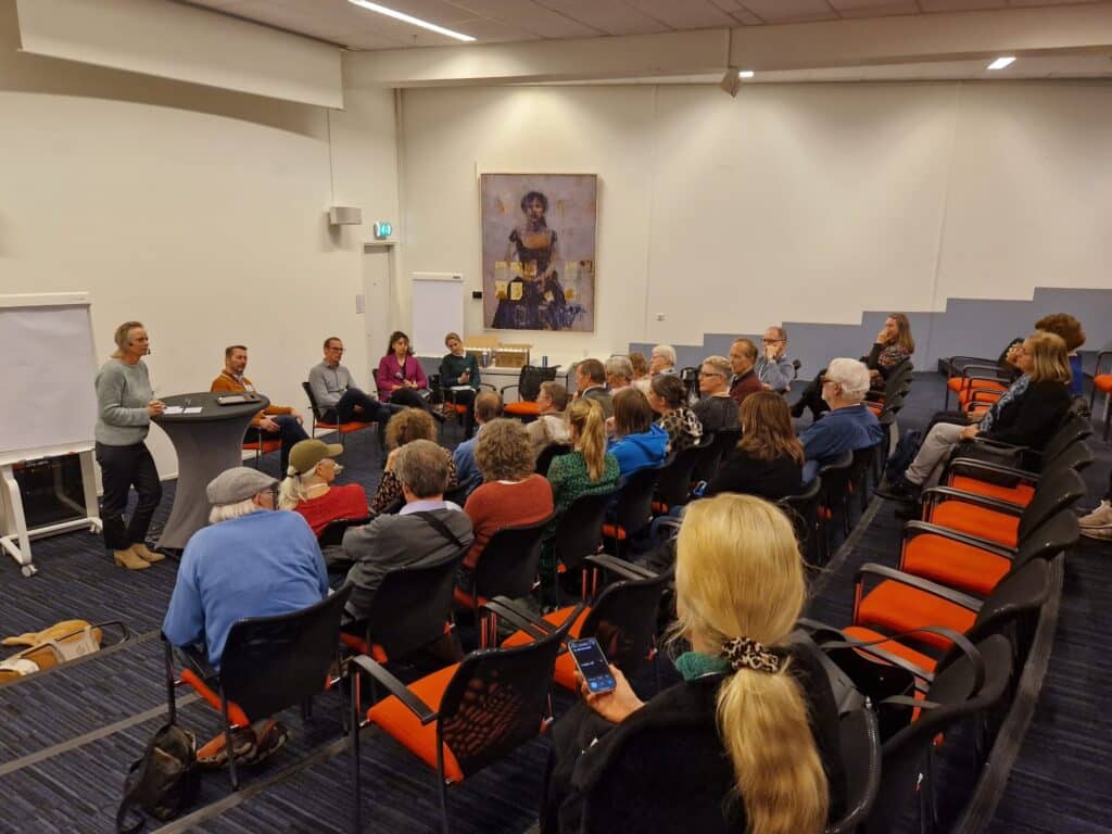 bezoekers in een grote auditorium zaal luisteren naar panelgesprek