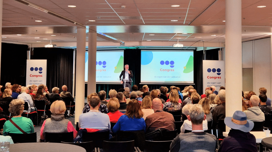 een volle zaal luistert naar directeur luuk-jan boon die het oogcongres opent op het podium