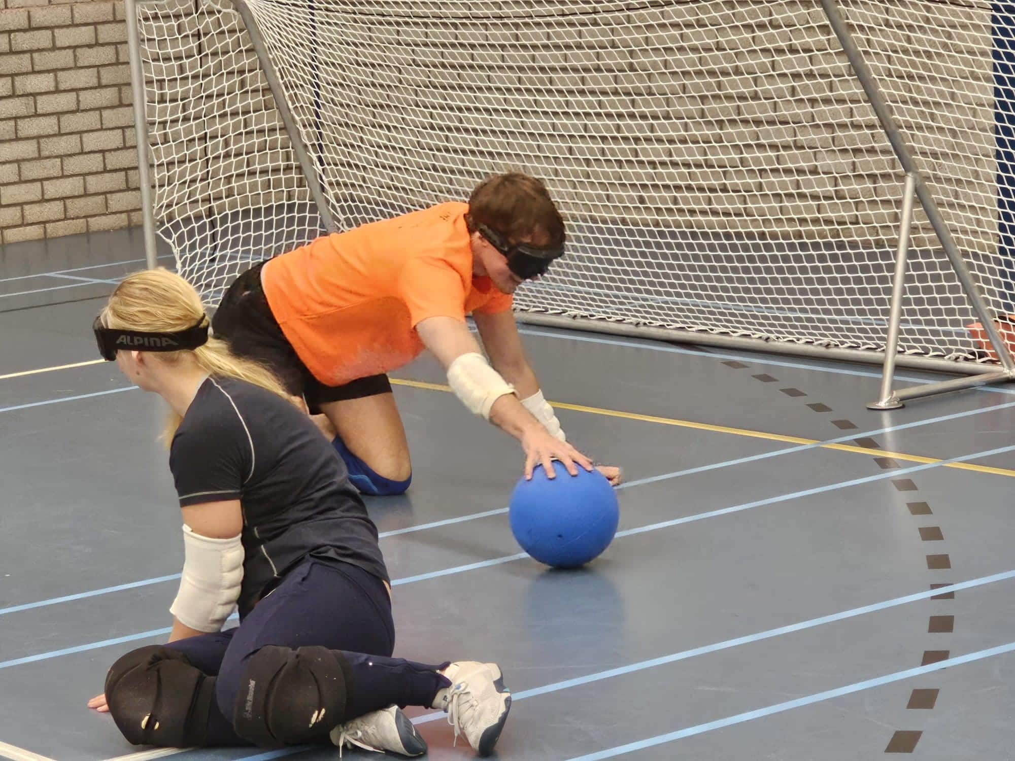 een goalballer stopt een bal, kruipend voor het doel