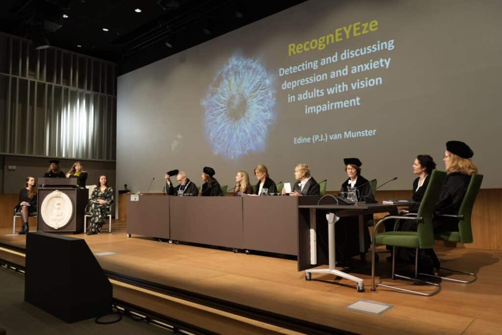 promovendi in zwarte toga's zitten op een een podium