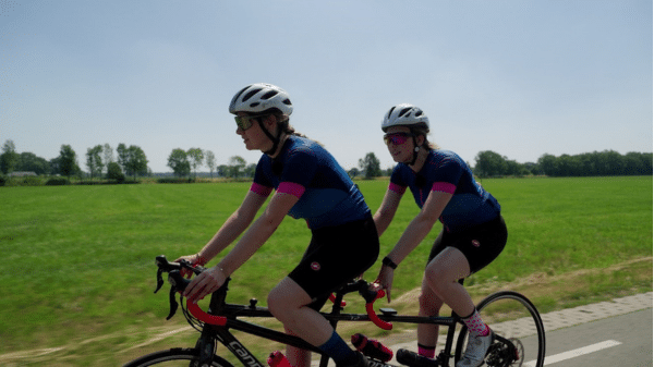 twee dames in de zon op een tandem in een fietspak met een helm op