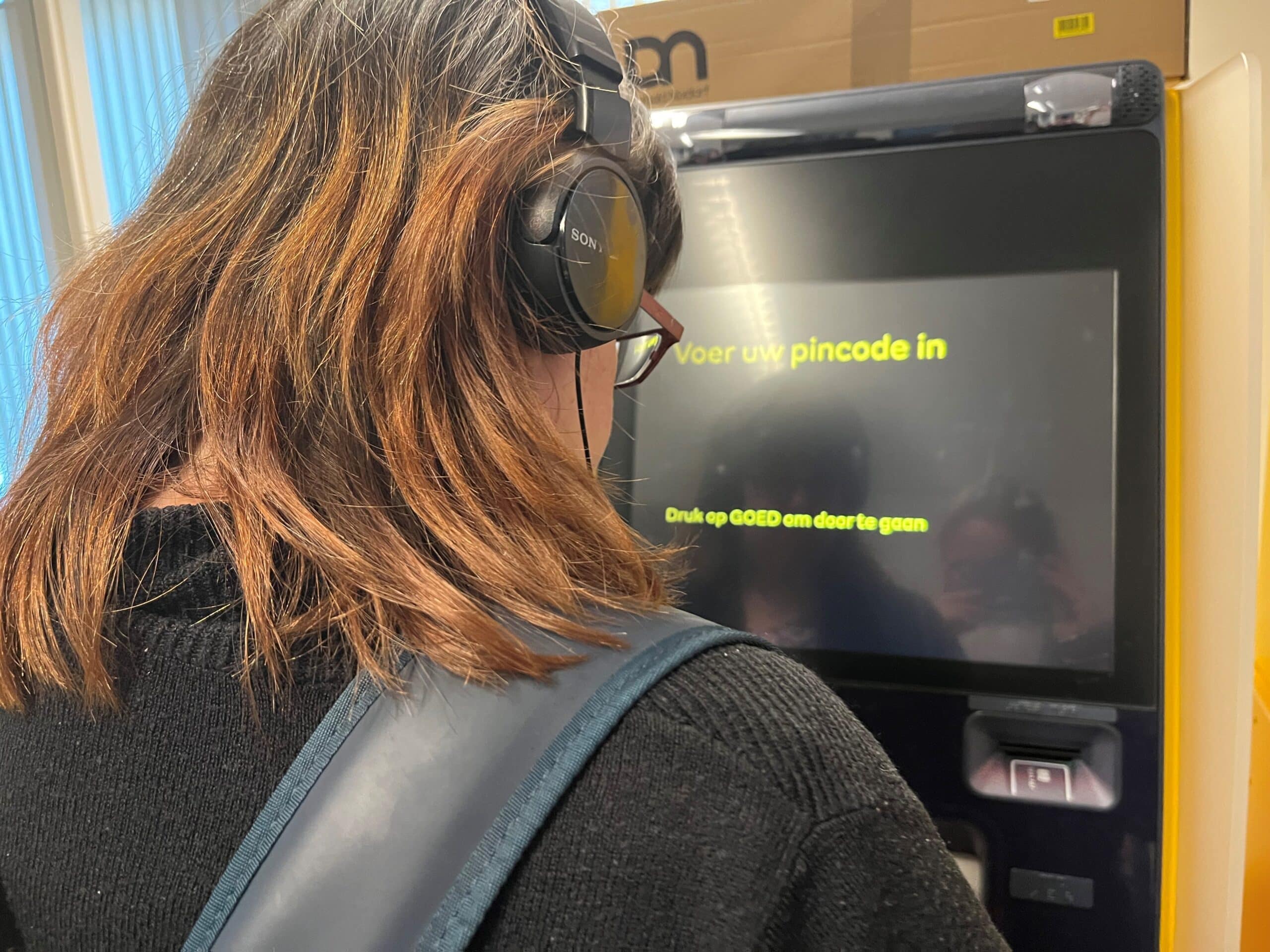 een vrouw met koptelefoon op, luistert naar de instructies van een geldmaat pinautomaat