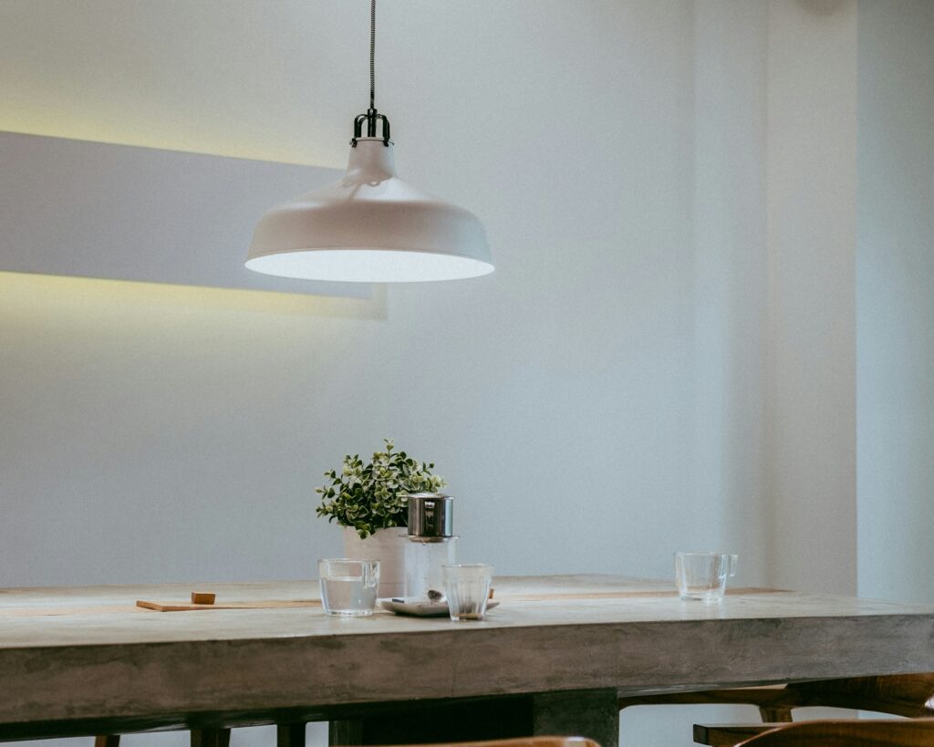 een brede witte hanglamp brandt boven een lange tafel