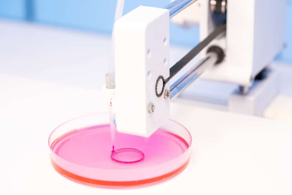 een voorbeeldfoto van een bioprinter die in een klein bakje een roze materie aan het uitspuwen is