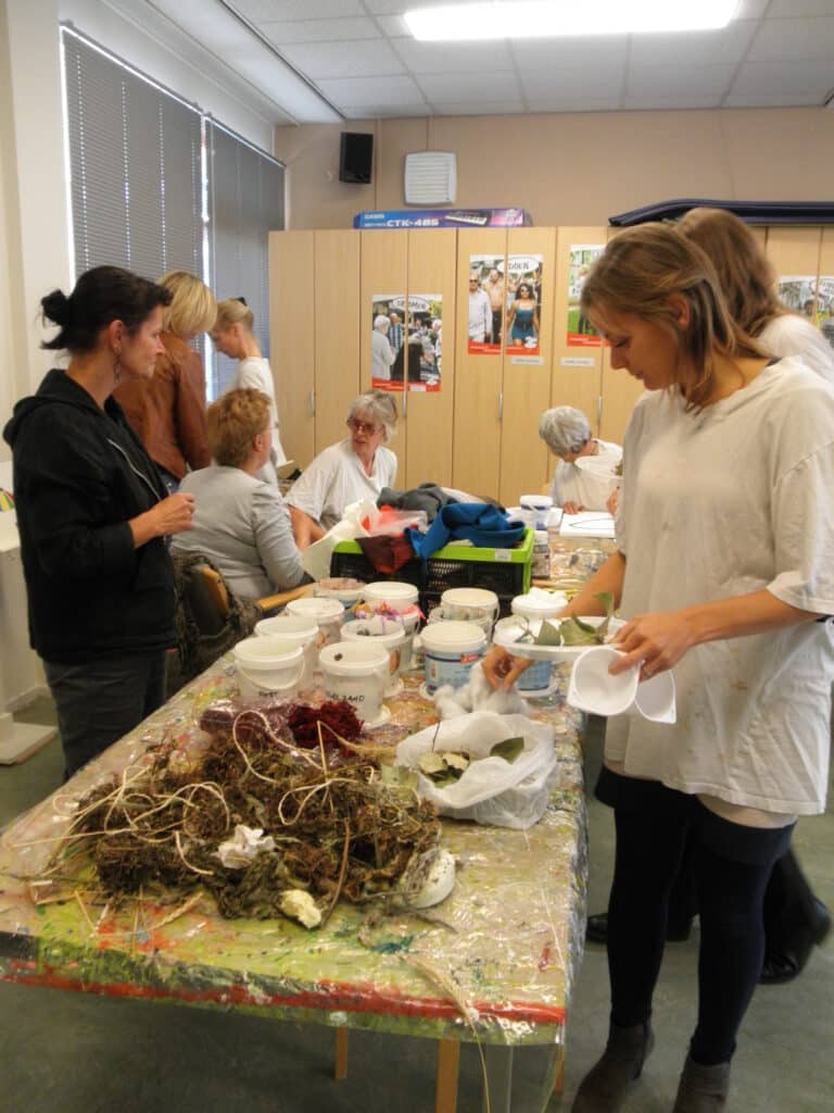 deelnemers van de workhop voelbare schilderijen maken zoeken in plastic bakken naar bruikbare materialen