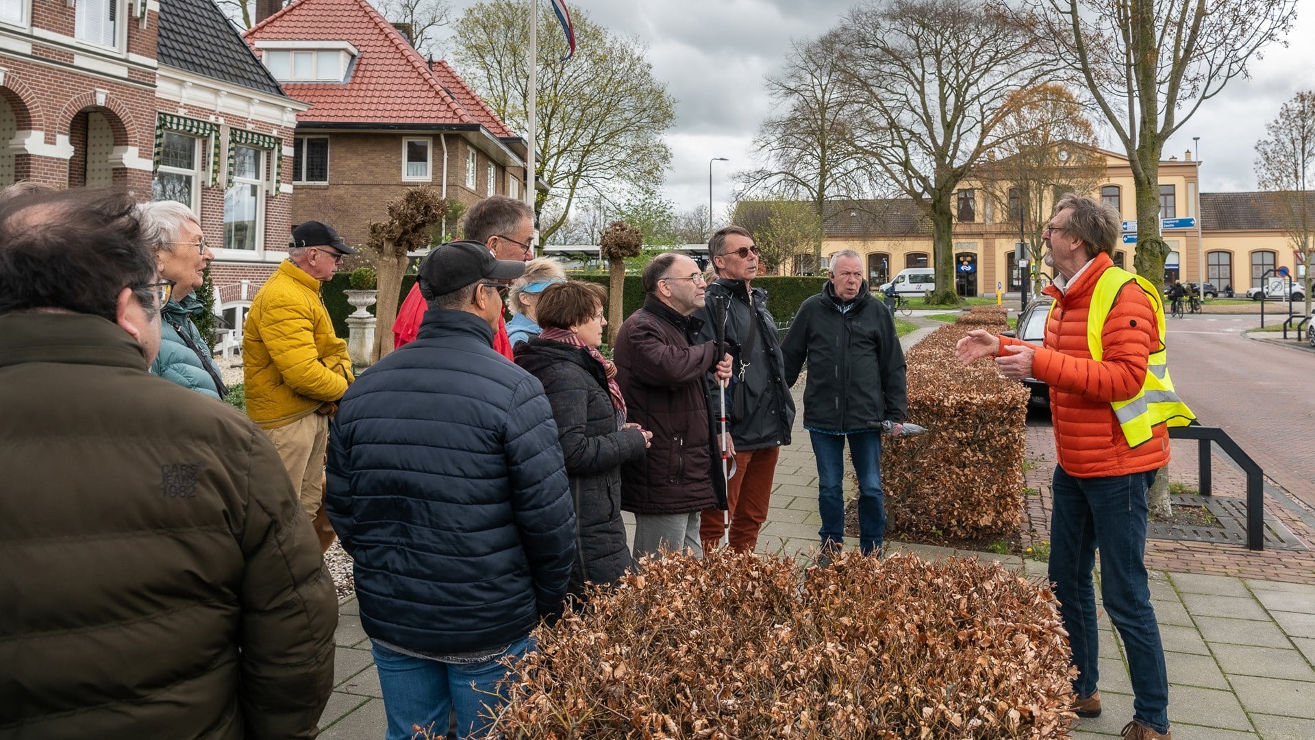 een groep wandelaars luistert naar het verhaal van de gids, op de achtergrond zien we de oude stationshal van Meppel