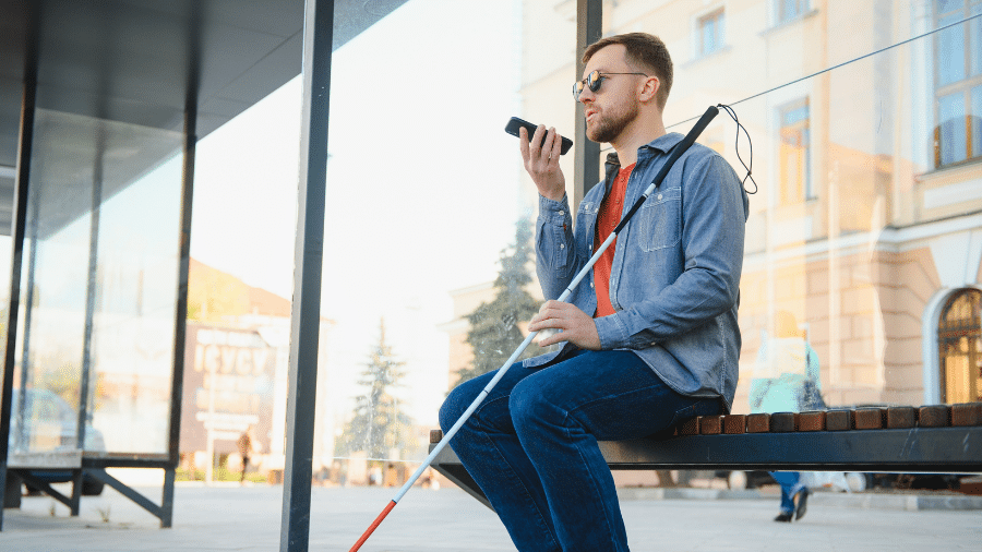 een jongeman praat tegen zijn smartphone op het bankje van de bushalte