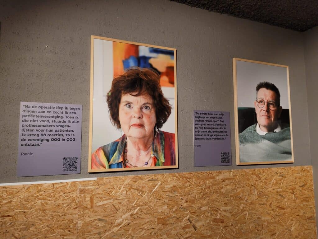 twee portretten hangen in een expositieruimte. . op de foto's zijn een man en vrouw geportretteerd in hun thuisomgeving. daarnaast hangen bordjes met achtergrondverhalen en een qr-code