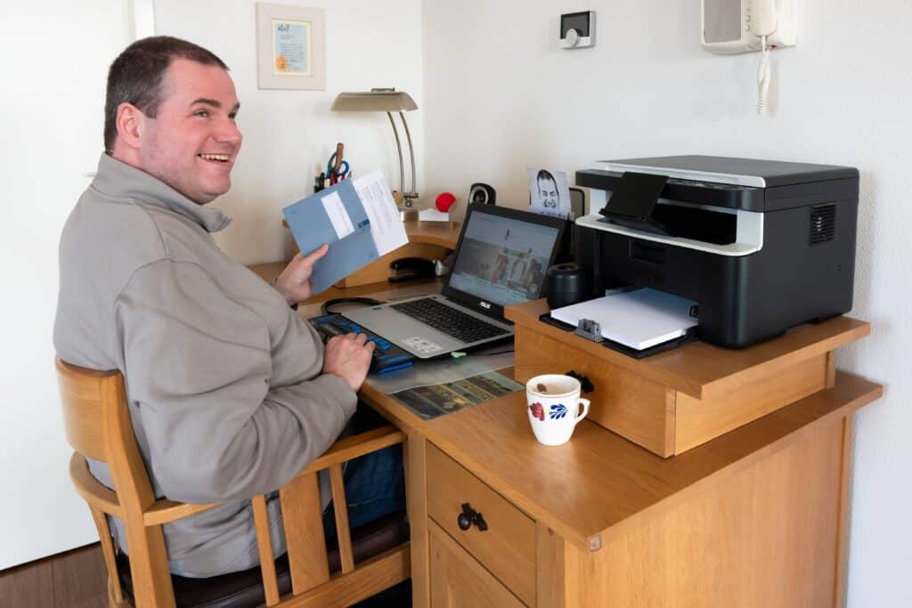 Ralf Habets achter een bureau, hij werkt op zjin laptop met leesregel. LInks van hem liggen blauwe enveloppen van de Belastingdienst