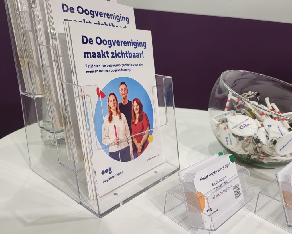 een statafel met verschillende promotiematerialen van de Oogverenigng, zoals een brochure, Ooglijnkaartjes en sleutelhangers in de vorm van een witte stok