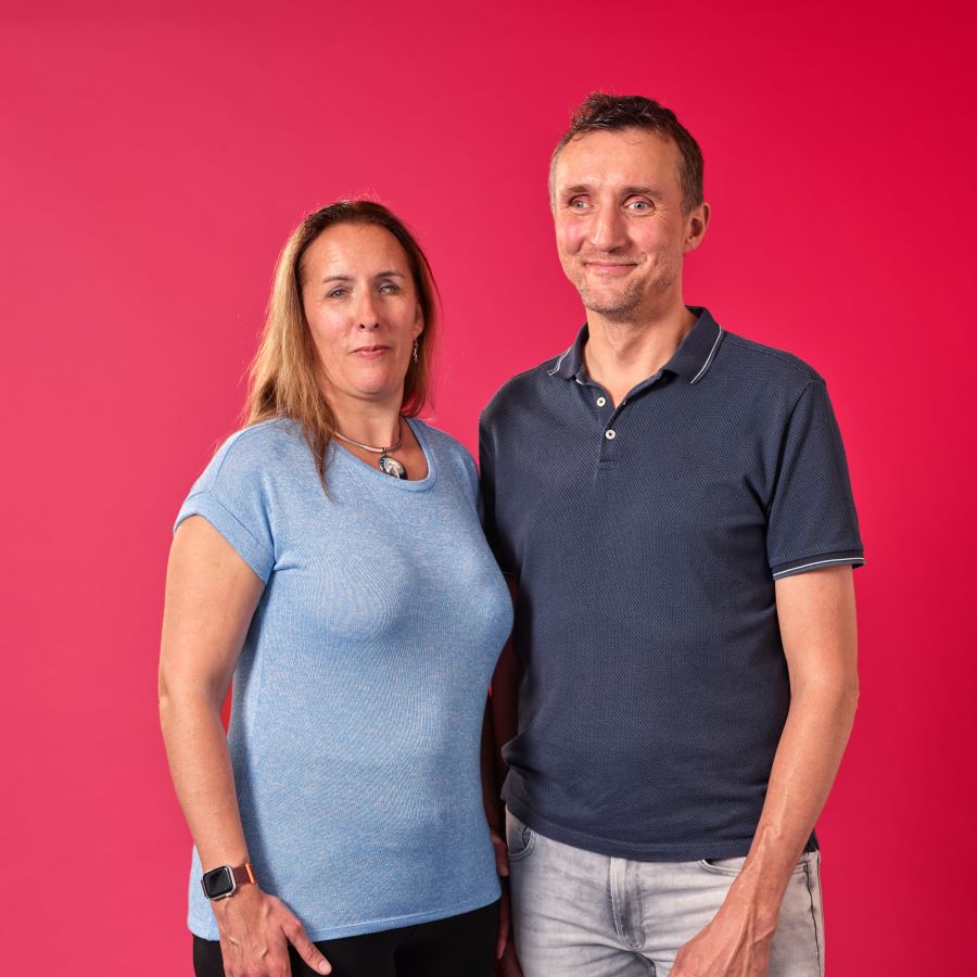 Een portretfoto van een vrouw en man met een visuele beperking. Ze lachen naar de camera, de achtergrond is rood