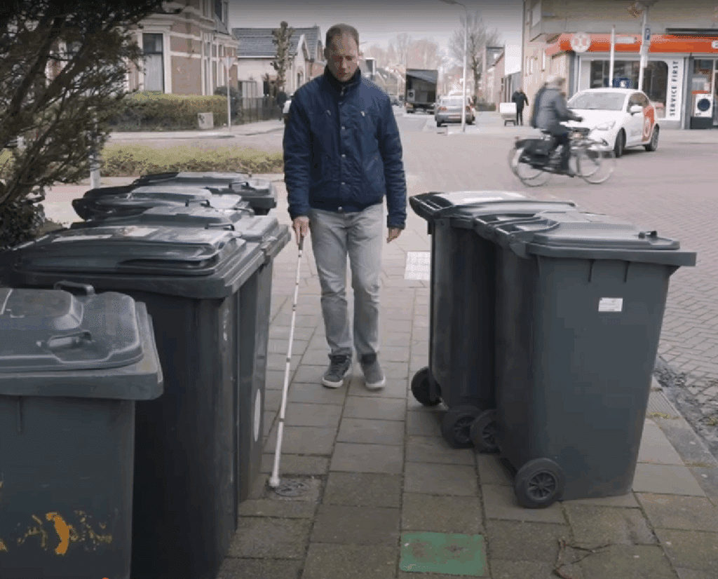 een witte stokloper baant zich over de stoep door een verzameling containers