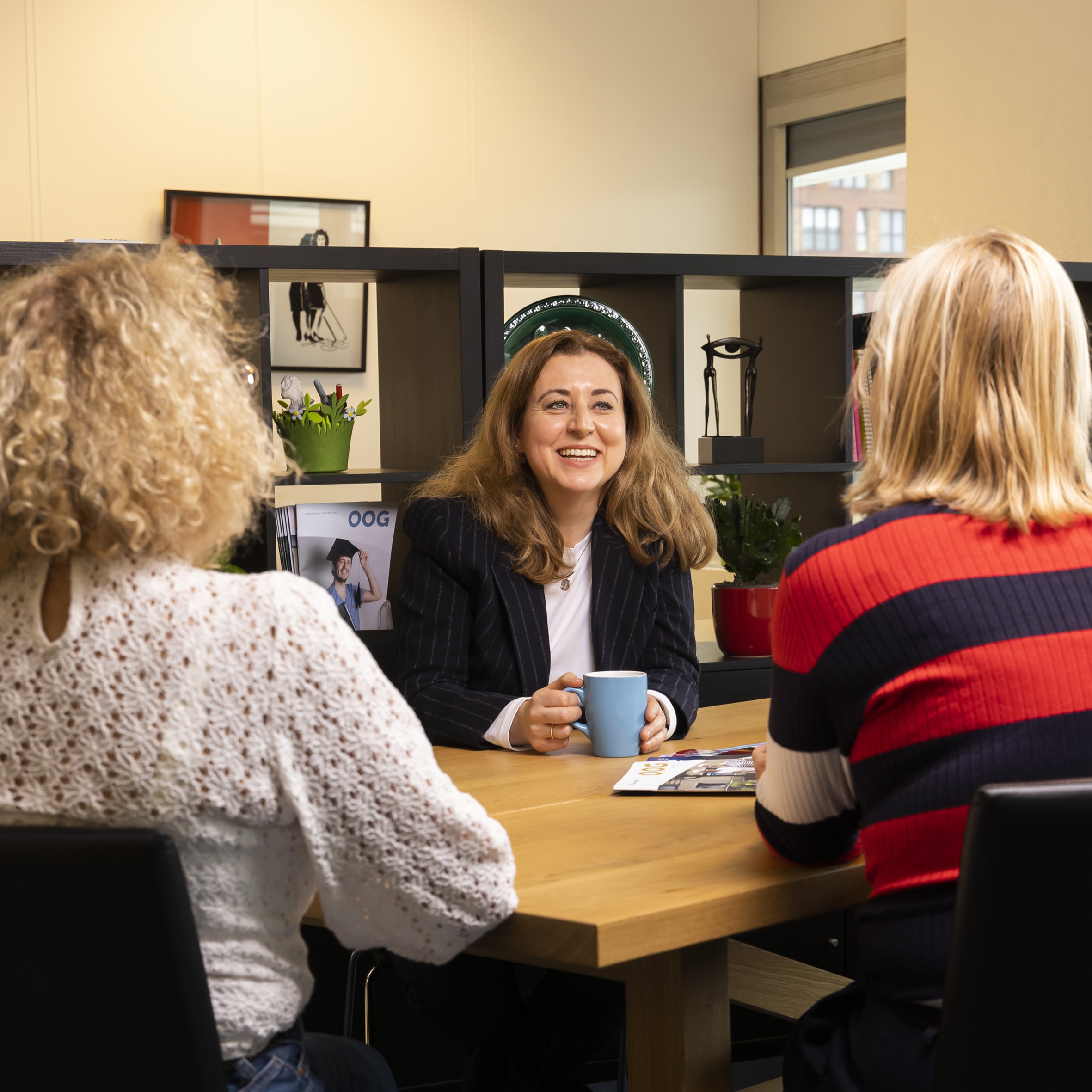 Drie vrouwen zitten aan een tafel en drinken koffie