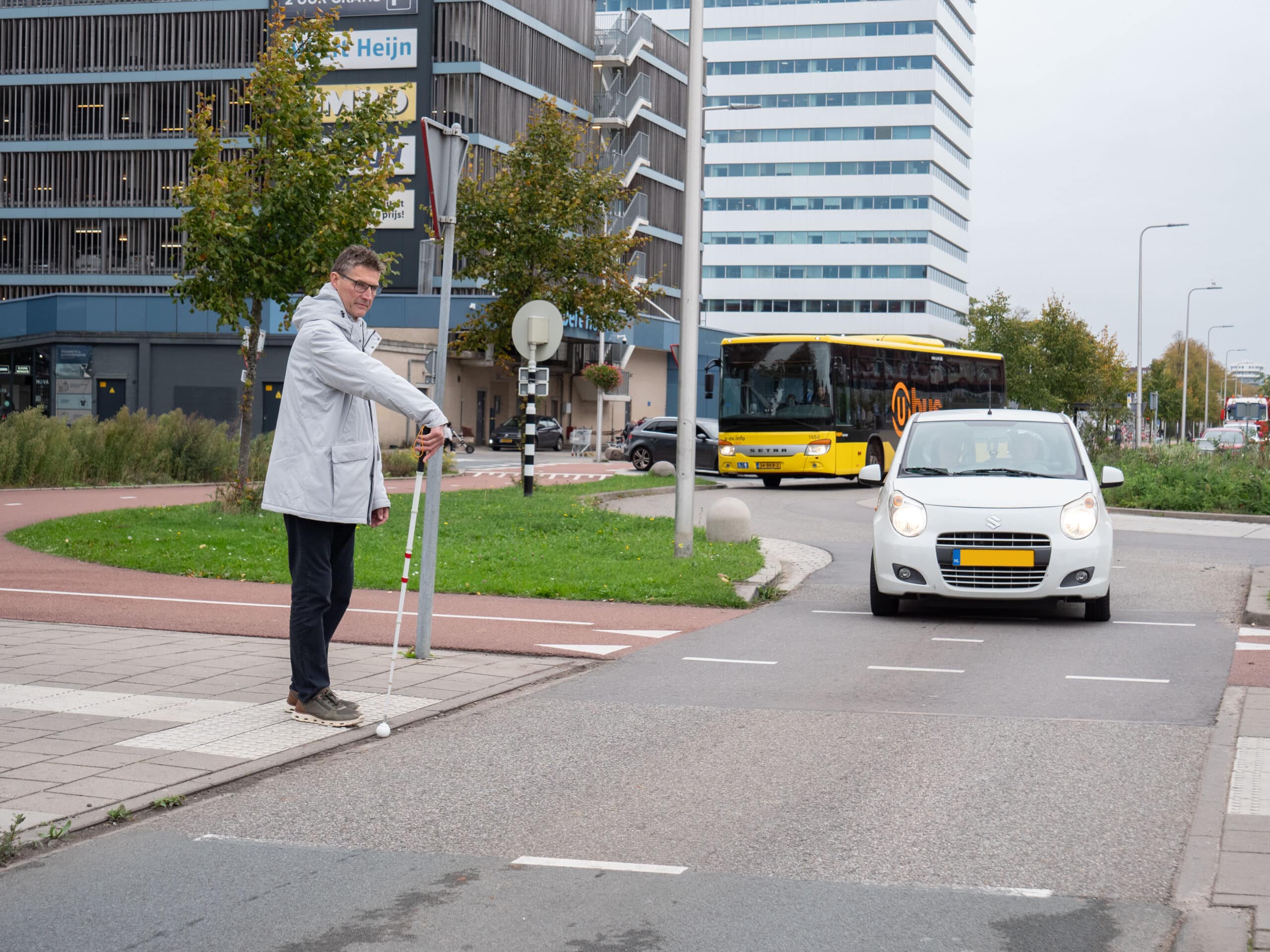 een man met witte stok maakt een stopgebaar, een auto die de rotonde verlaat verleent voorrang