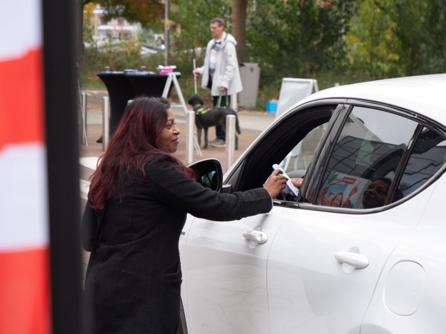 Een medewerkster van de Oogvereniging geeft door het autoraam een parkeerschijf aan een automobilist