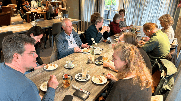 deelnemers van de deelgnotendag kletsen aan een lange tafel met koffie, thee en taart met slagroom