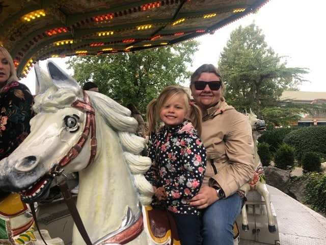 een vrouweiljke deelnemer met een jong meisje op de rug van een hobbelpaard van de draaimolen in Ponypark Slagharen.