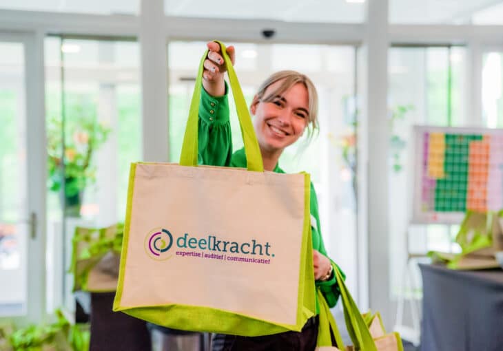 een lachende jongedame ze laat een tasje zien met het deelkracht logo