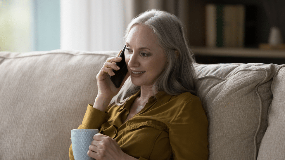 een vrouw belt met haar smartphone, ze zit met koffie op de bank