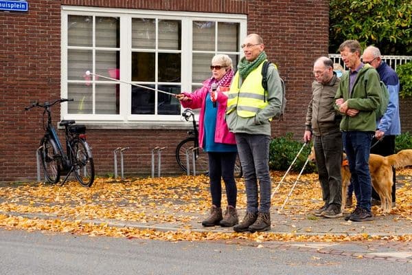 een vrijwilliger helpt iemand met een witte stok bij het oversteken