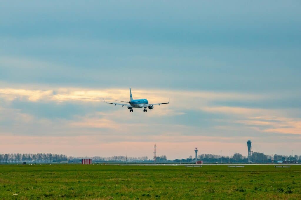 een KLM vliegtuig zet de landing in, ondergaande zon op de achtergrond