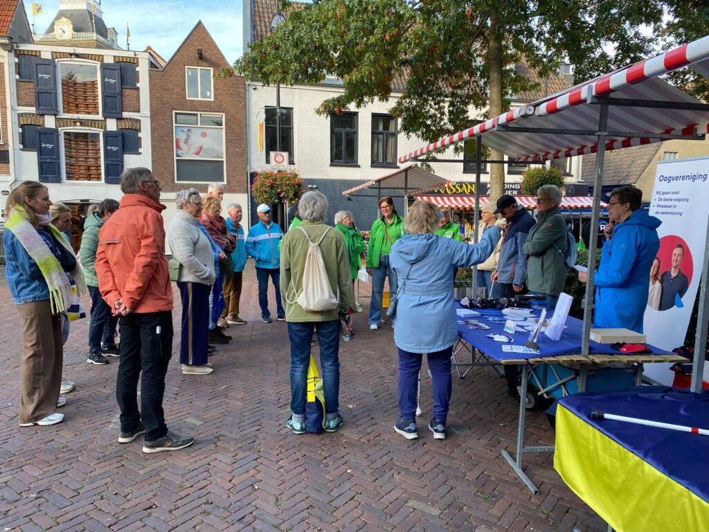 Een groep mensen verzamelt zich rond een marktkraam van de Oogvereniging op een plein in Meppel.