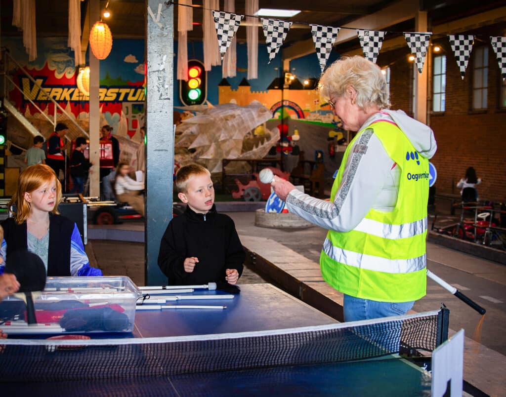 ervaringsdeskundige met Oogvereniging hesje laat een witte stok zien aan twee jonge kinderen
